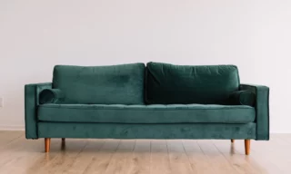 emerald green couch on a living room with a wood floor and white walls